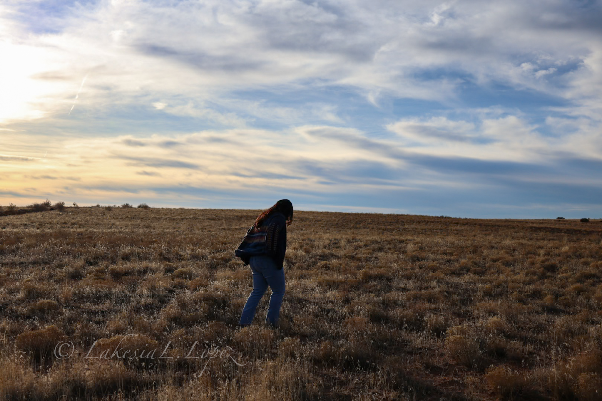 Person walking through an open field beneath a wide sky